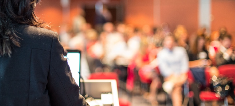 A woman professor stands behind a podium and teaches college students