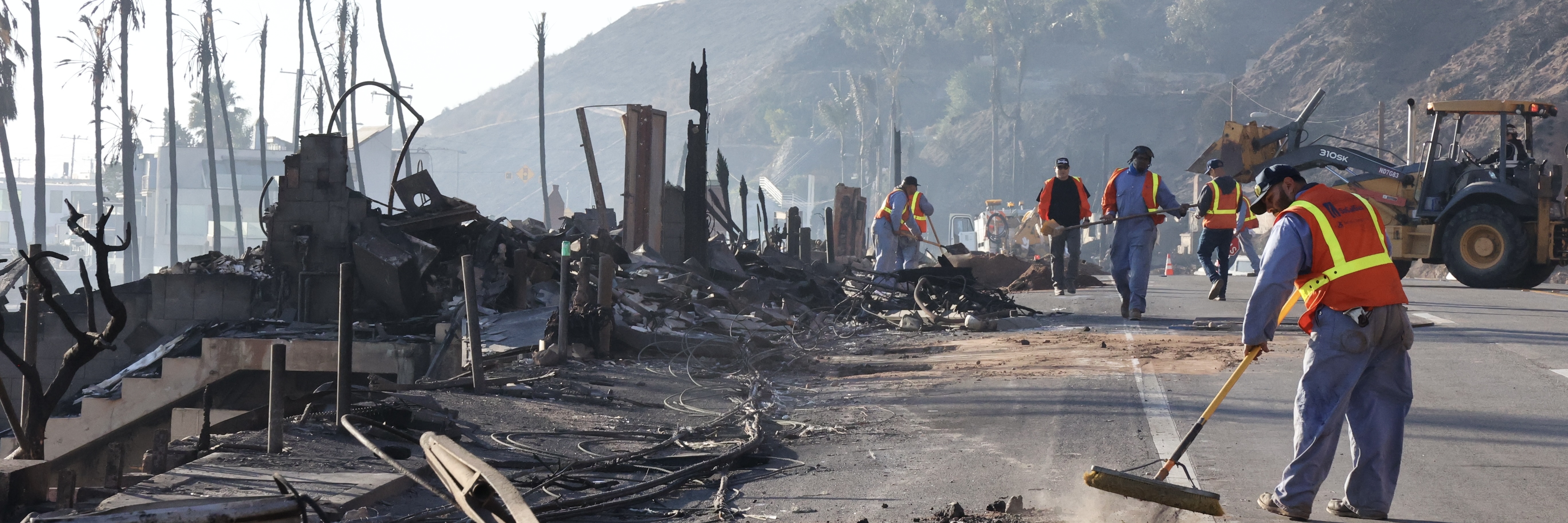 A clean-up crew sweeps ash and clears debris from the Palisades Fire on January 11, 2026.